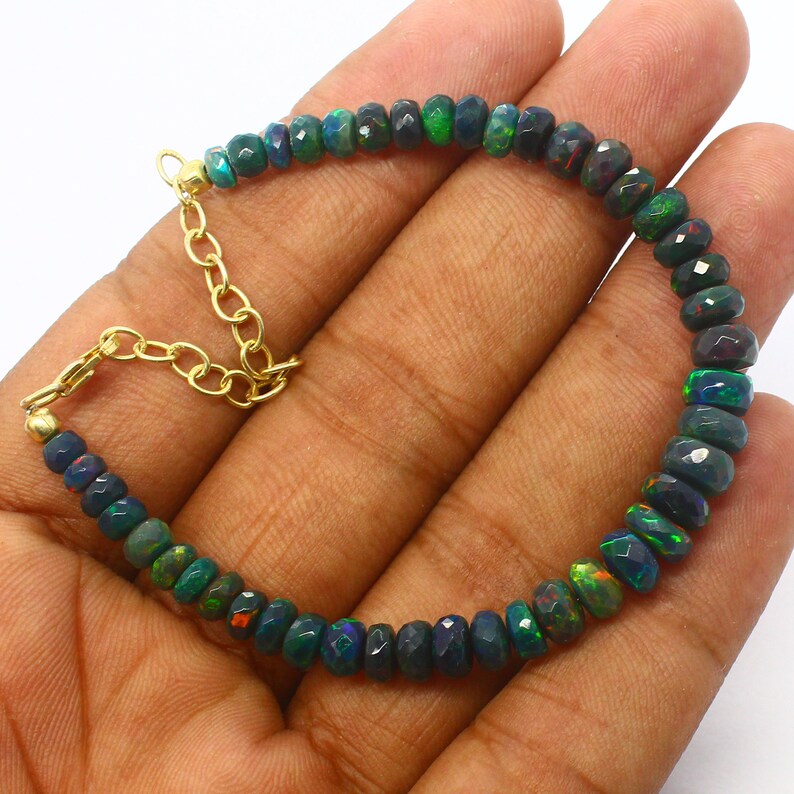 May include: A black opal beaded bracelet with a gold chain clasp. The beads are faceted and have a dark green, blue, and red iridescent sheen.