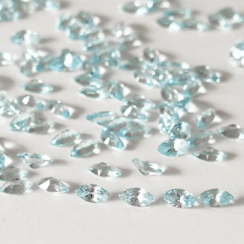 May include: A scattering of light blue marquise-shaped gemstones on a white surface.