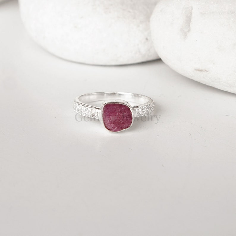 Peut inclure: Une bague en argent avec une pierre pr&eacute;cieuse rose sertie dans une forme carr&eacute;e. La bande de la bague est d&eacute;cor&eacute;e de petites pierres blanches.