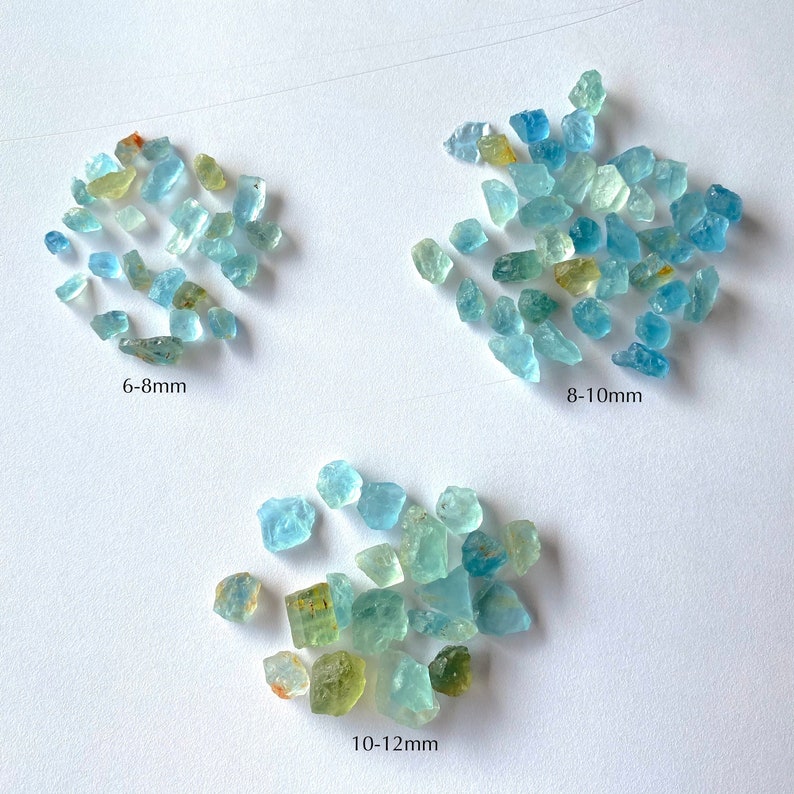 Pode incluir: Tr&ecirc;s grupos de pedras preciosas de &aacute;gua-marinha bruta, classificadas por tamanho. Os grupos s&atilde;o etiquetados como 6-8 mm, 8-10 mm e 10-12 mm.