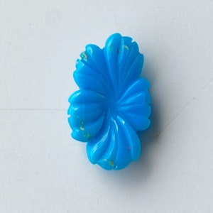 May include: A bright blue flower-shaped cabochon with a carved design. The cabochon has a slightly mottled appearance with flecks of white and gold.