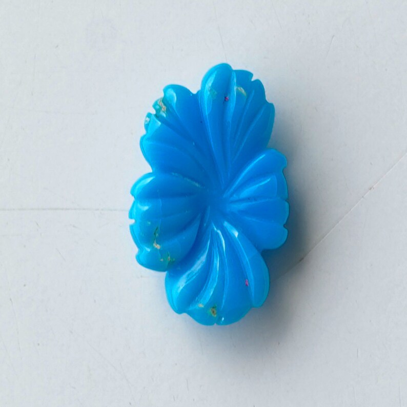 May include: A bright blue flower-shaped cabochon with a carved design. The cabochon has a slightly mottled appearance with flecks of white and gold.
