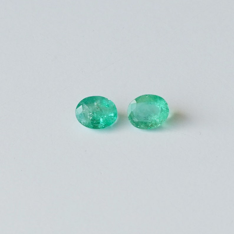 May include: Two round, green emerald gemstones on a white background.
