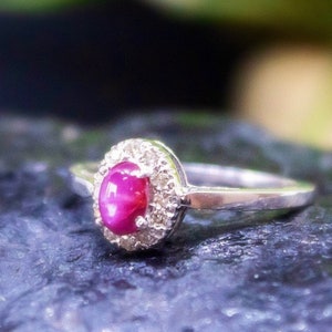 Può includere: Un anello d'argento con una pietra preziosa di rubino rosa circondata da un'aureola di diamanti più piccoli.