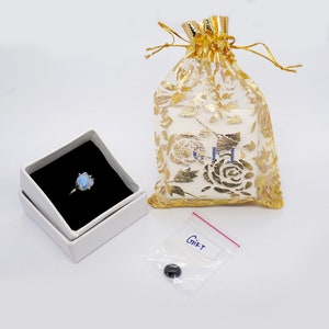 May include: A silver ring with a blue gemstone in a white box, a gold drawstring bag, and a small plastic bag with a black stone and the word "Gift" written on it.