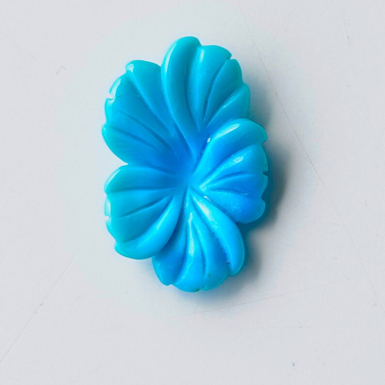 May include: A bright blue carved flower shaped cabochon. The flower has five petals and is made of a smooth, polished material.