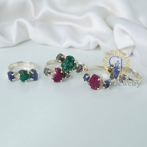 Peut inclure: Trois bagues en argent serties de pierres précieuses brutes. Les bagues présentent une émeraude verte, un rubis rouge et un saphir bleu. Chaque bague possède également un petit diamant noir.