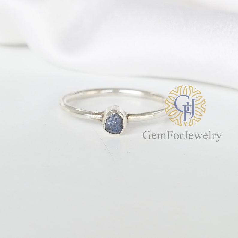 May include: A silver ring with a small, rough, blue gemstone set in the center.
