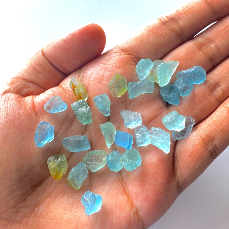 Pode incluir: Uma cole&ccedil;&atilde;o de gemas de &aacute;gua-marinha bruta em v&aacute;rios tons de azul e verde. As gemas s&atilde;o brutas e t&ecirc;m um acabamento natural n&atilde;o polido.