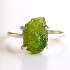 Könnte beinhalten: Ein Silberring mit einem rohen, grünen Peridot-Edelstein, der in einer Krappenfassung sitzt.