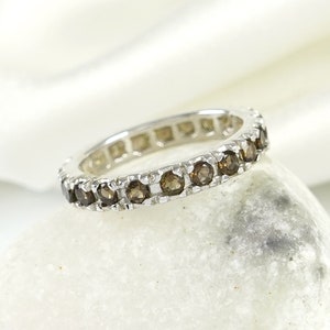 May include: A silver band ring with a row of brown gemstones. The ring is on a white surface.