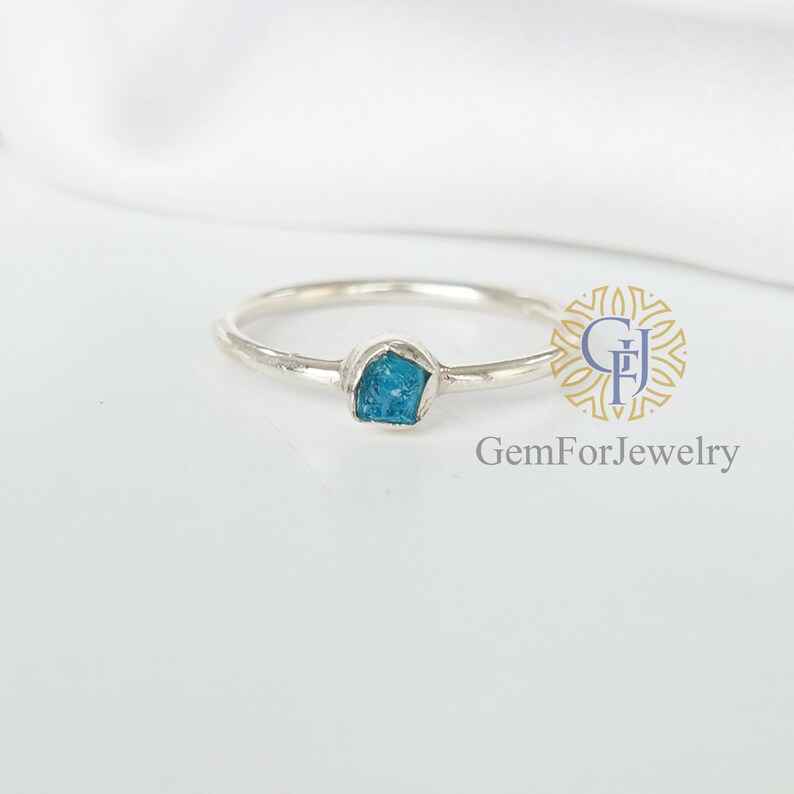 May include: A silver ring with a small, blue, rough-cut gemstone. The ring is simple and delicate.