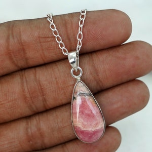 May include: A silver necklace featuring a teardrop-shaped pendant. The pendant has a pink and white stone with a silver bezel. The chain is made of small, linked silver pieces. The necklace is displayed against a neutral background.