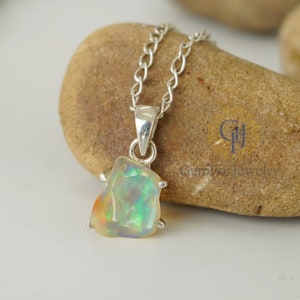 May include: A silver chain necklace with a pendant featuring a raw opal gemstone. The opal is a light green, white, and orange colour with iridescent flashes.