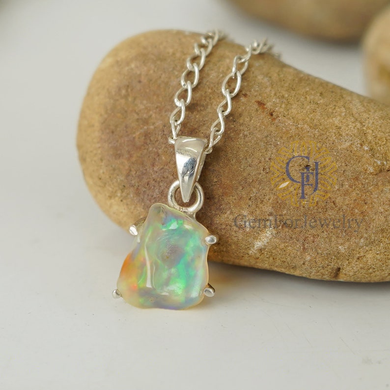 May include: A silver chain necklace with a pendant featuring a raw opal gemstone. The opal is a light green, white, and orange colour with iridescent flashes.