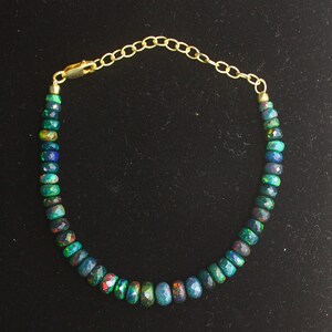May include: A gold chain bracelet with a row of dark green, blue, and red opal beads.