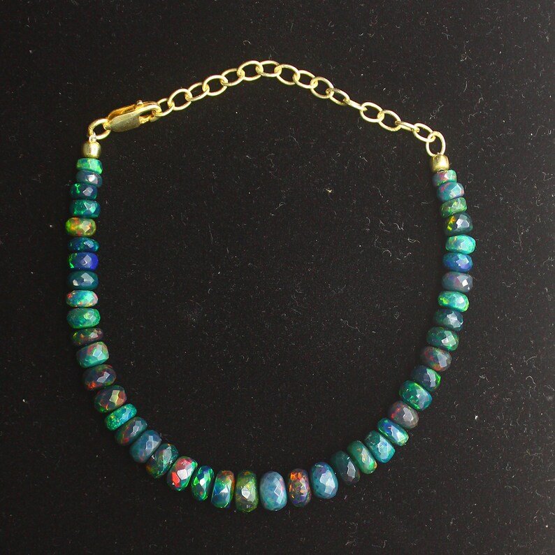May include: A gold chain bracelet with a row of dark green, blue, and red opal beads.