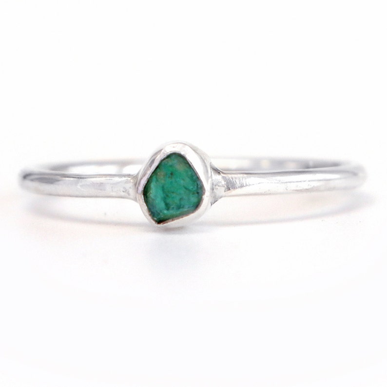 May include: A silver ring with a rough, green emerald gemstone set in the center.