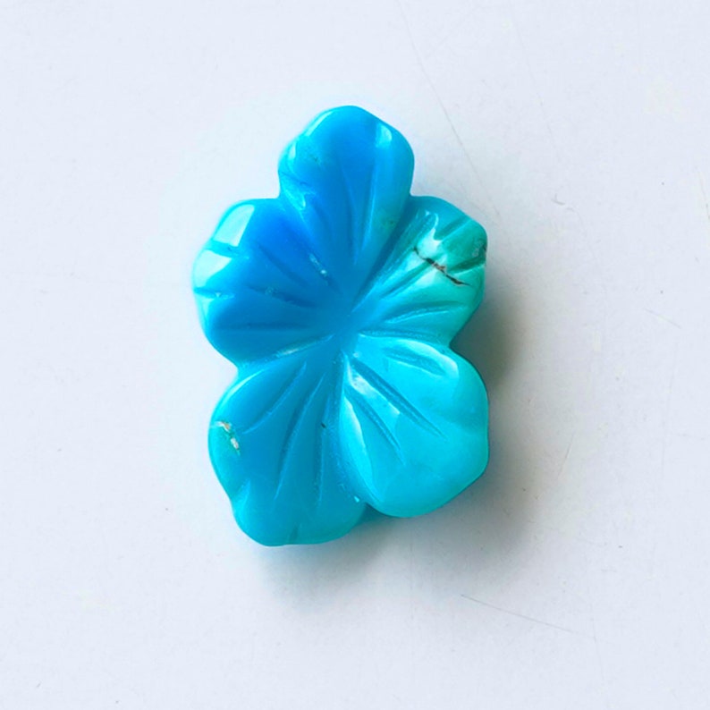 May include: A turquoise blue flower-shaped cabochon gemstone. The stone has a carved design and is a light blue color.