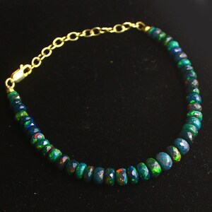 May include: A gold chain bracelet with a series of dark green and black opal beads. The beads are faceted and have a rainbow sheen.