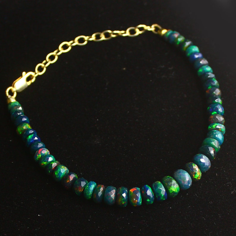 May include: A gold chain bracelet with a series of dark green and black opal beads. The beads are faceted and have a rainbow sheen.