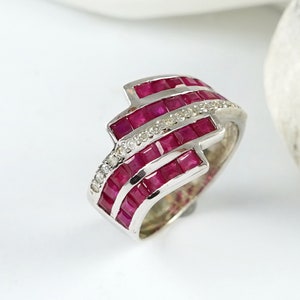 Op de afbeelding: Een zilveren ring met drie rijen vierkante robijnen en een rij kleinere, ronde diamanten.