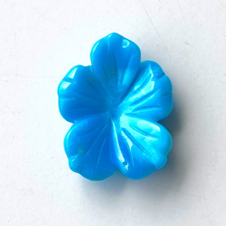 May include: A bright blue flower-shaped cabochon, carved from turquoise, with a smooth, polished surface.