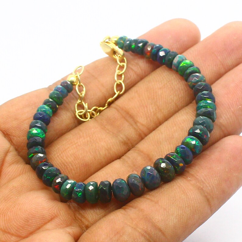 May include: A green and black opal gemstone bracelet with a gold clasp. The bracelet is made of round, faceted beads.