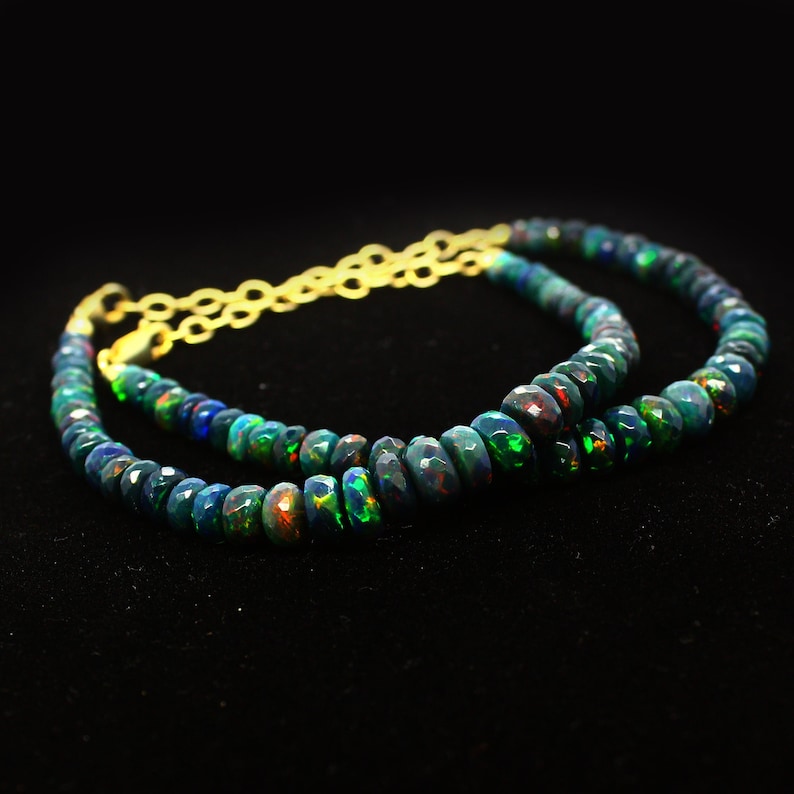 May include: A double strand necklace made of black opal beads with a gold chain clasp. The beads are faceted and have a green and red iridescent sheen.