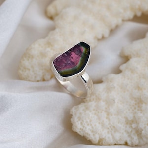 K&ouml;nnte beinhalten: Ein Silberring mit einem Wassermelonen-Turmalin-Edelstein. Der Edelstein zeigt einen Farbverlauf von Rosa, Gr&uuml;n und Schwarz. Der Ring hat ein poliertes Silberband, und der Edelstein ist in einer Zargenfassung gefasst.