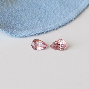 May include: Two pear-shaped pink gemstones on a white background.