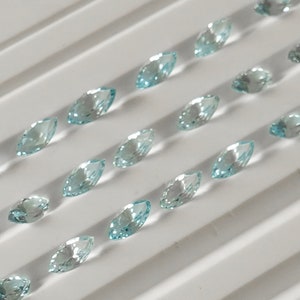 May include: A collection of light blue marquise-shaped gemstones arranged in rows on a white background.