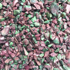 May include: A close-up of a pile of small, rough, green and pink gemstones. The stones are irregularly shaped and have a natural, unpolished look.