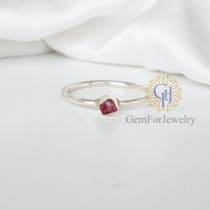 May include: A silver ring with a small, rough, pink gemstone set in the center.