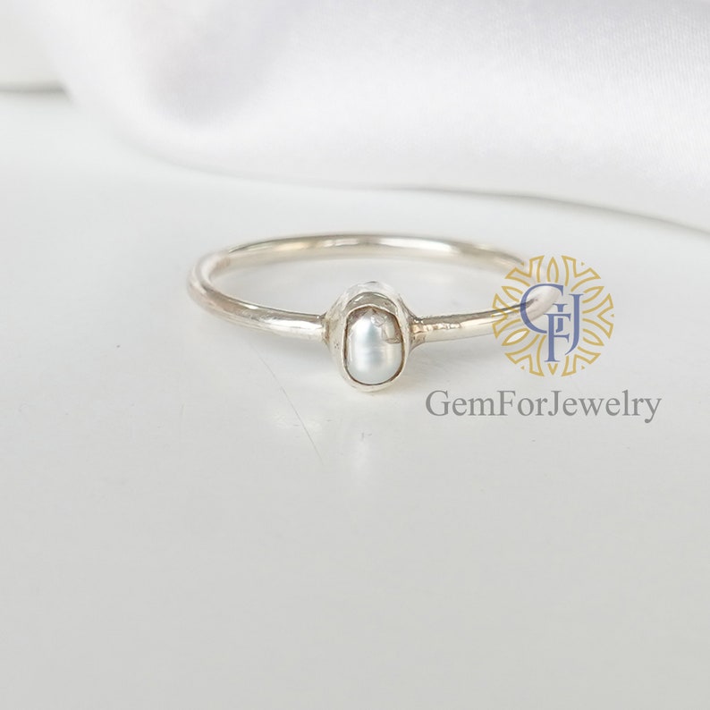 May include: A delicate silver ring with a single white pearl set in a bezel setting. The ring is simple and elegant, perfect for everyday wear.