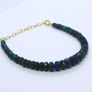 May include: A green opal gemstone bracelet with a gold chain clasp. The bracelet is made of faceted beads and has a dark green color with flashes of blue and rainbow.