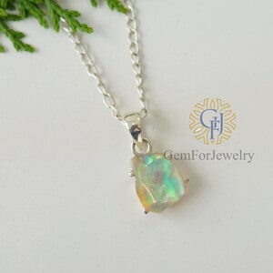 May include: A silver chain necklace with a pendant featuring a raw, iridescent opal stone. The opal is set in a silver bezel and has a natural, irregular shape.