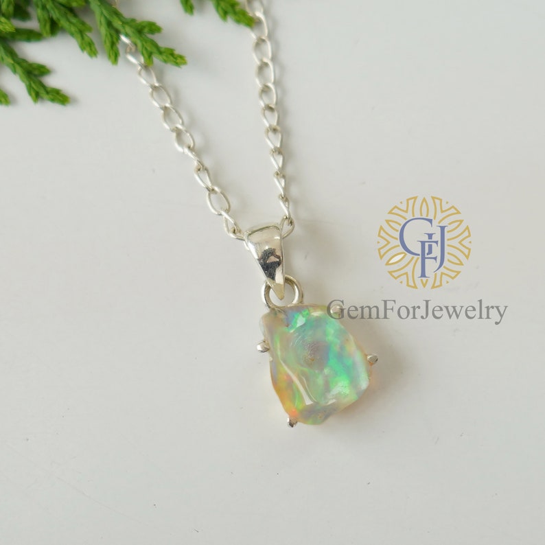 May include: A silver chain necklace with a pendant featuring a raw, iridescent opal stone. The opal is set in a silver bezel and has a natural, irregular shape.