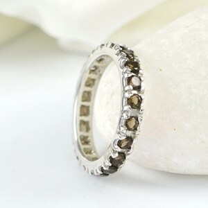 May include: A silver band ring with a row of brown gemstones. The ring is set on a white background.