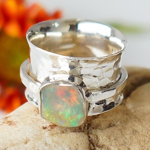 May include: A silver ring with a hammered band and a large, iridescent opal gemstone. The ring is designed to be worn as a spinner ring.