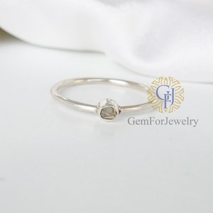 May include: A simple silver ring with a small, clear, faceted gemstone set in the center.