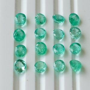 May include: A collection of 15 round, faceted, green gemstones. The gemstones are arranged in rows on a white surface.