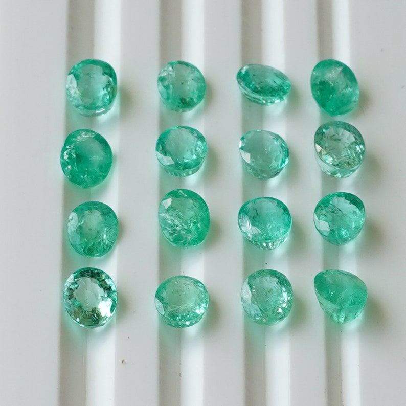 May include: A collection of 15 round, faceted, green gemstones. The gemstones are arranged in rows on a white surface.