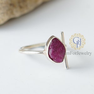 K&ouml;nnte beinhalten: Ein silberner Ring mit einem rohen Rubin-Edelstein und einem silbernen Balken-Akzent. GemForJewelry ist im Hintergrund gedruckt.