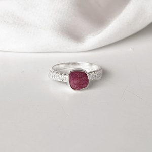 Peut inclure: Une bague en argent avec une pierre pr&eacute;cieuse rose sertie dans une forme carr&eacute;e. La bande de la bague est d&eacute;cor&eacute;e de petites perles d'argent.