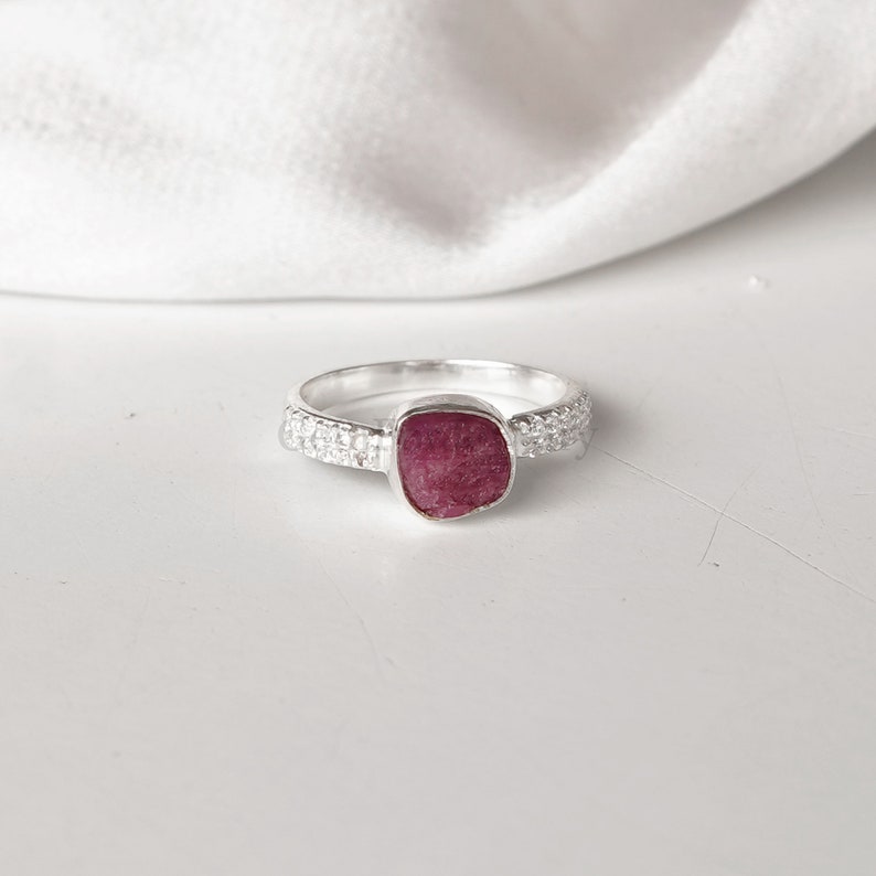 Peut inclure: Une bague en argent avec une pierre pr&eacute;cieuse rose sertie dans une forme carr&eacute;e. La bande de la bague est d&eacute;cor&eacute;e de petites perles d'argent.