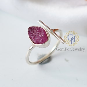 K&ouml;nnte beinhalten: Ein silberner Ring mit einem rosafarbenen Rubin-Edelstein, der in einer Zargenfassung gefasst ist. Der Ring hat eine silberne Leiste, die &uuml;ber die Oberseite des Rings verl&auml;uft.