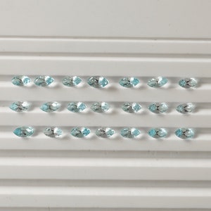 May include: A tray of 20 light blue marquise-shaped gemstones. The gemstones are arranged in four rows of five.