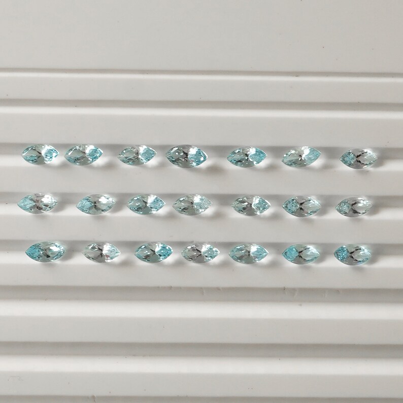 May include: A tray of 20 light blue marquise-shaped gemstones. The gemstones are arranged in four rows of five.