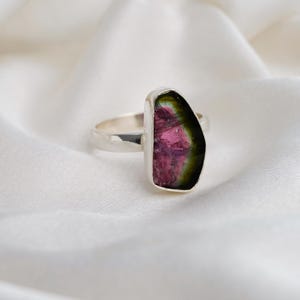 K&ouml;nnte beinhalten: Ein Silberring mit einem rohen Wassermelonen-Turmalin-Edelstein. Der Stein hat rosa, gr&uuml;ne und schwarze Farbt&ouml;ne. Das Band des Rings ist ein schlichtes, poliertes Design. Der Edelstein hat eine einzigartige, nat&uuml;rliche Form.